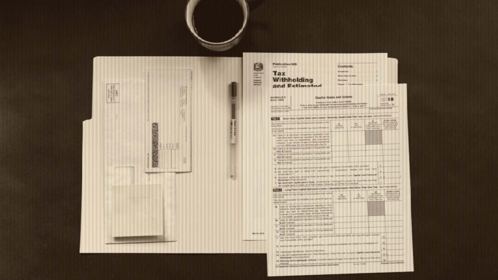 Tax forms, a pen, and a coffee mug on a dark desk